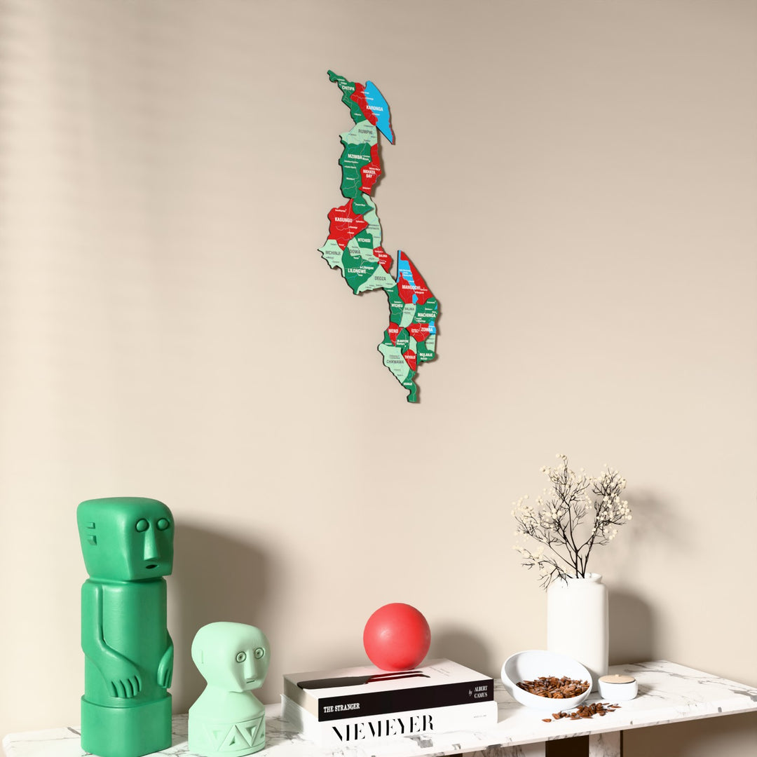 Flag colored Malawi wooden wall map on a beige wall above a console with figurines