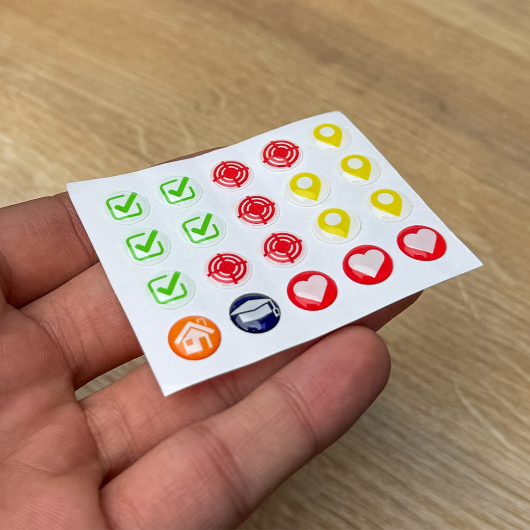 Sheet of 20 glossy map pins with check marks, targets, location markers, a house and a graduation cap, held in a hand