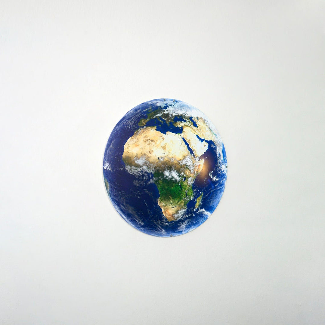 Round metal Earth wall art showing Africa and Europe on a light wall, straight-on view