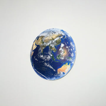 Small metal Earth wall art showing Asia and Australia on a light gray wall, angled view