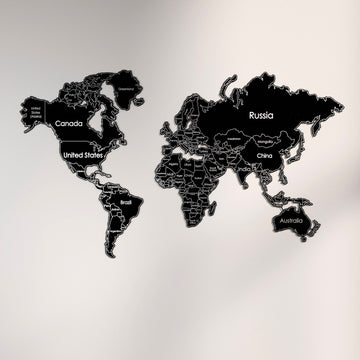 Black metal world map with white country outlines and names, front view on a light wall