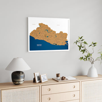 White framed El Salvador cork map on a gray wall above a sideboard with a lamp and framed photos