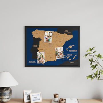 Black-framed Spain cork map with three pinned photos, hung beside a plant