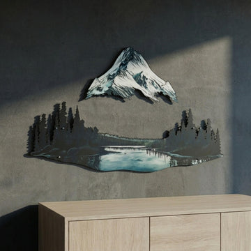Mountain and lake metal wall art with snowy peak and pine forest above a wooden sideboard