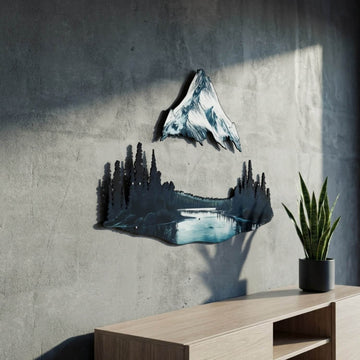 Mountain and lake metal wall decor at an angle, next to a snake plant