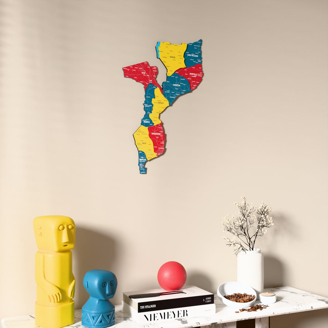 Flag colored Mozambique wooden wall map on a beige wall above a console with figurines