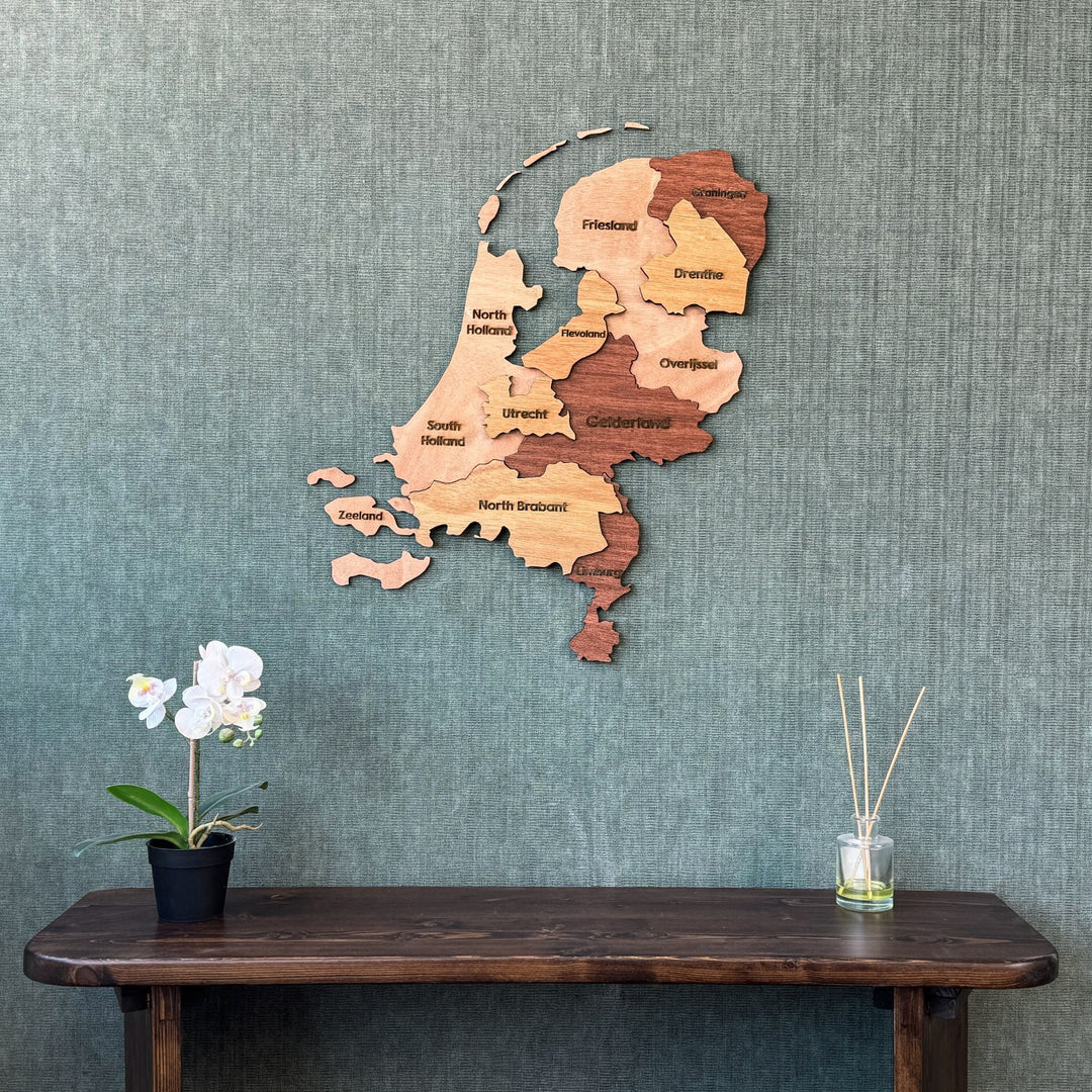 Wooden Netherlands map on a green textured wall above a dark console with an orchid