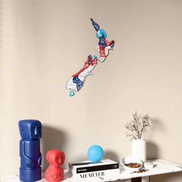 Flag colored New Zealand wooden wall map on a beige wall above a console with figurines