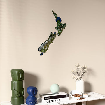 Satellite New Zealand wooden wall map on a beige wall above a console with figurines