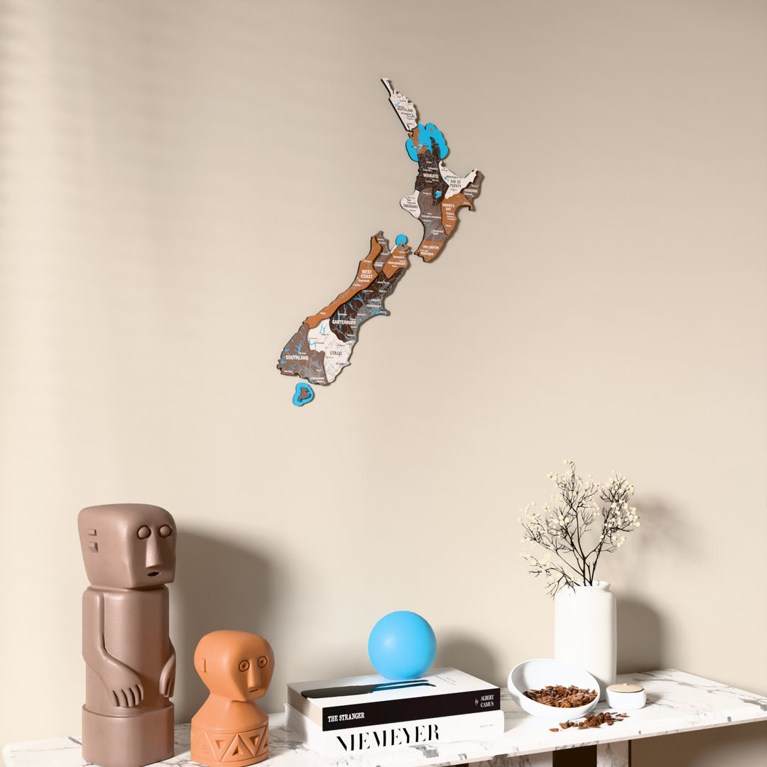 Soil New Zealand wooden wall map on a beige wall above a console with figurines
