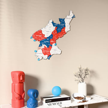 Flag colored North Korea wooden wall map on a beige wall above a console with figurines