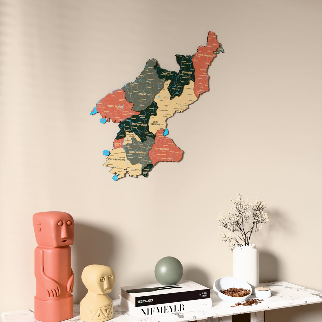 Sage North Korea wooden wall map on a beige wall above a console with figurines