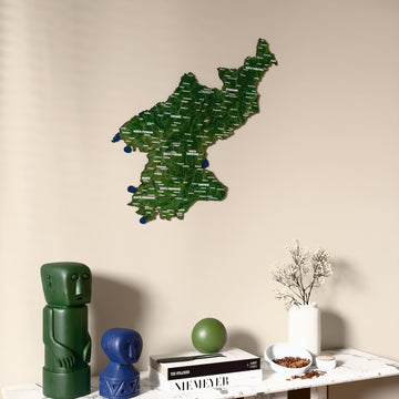 Satellite North Korea wooden wall map on a beige wall above a console with figurines