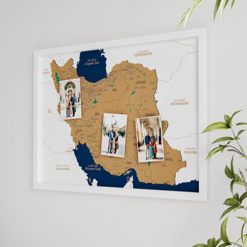 White-framed Iran cork map with three pinned photos, angled view from the left beside a plant