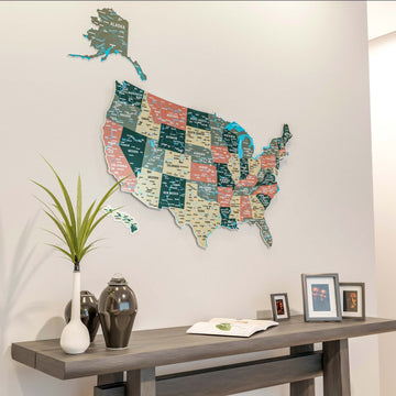 Large sage metal USA wall map from a slight angle, above a console with a white vase, dark jars and photo frames