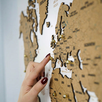 White cork world map, side view with Africa below as a hand places a gold pin on Europe