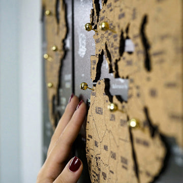 Black cork world map, side view of the cork surface as a hand pushes in a gold pin