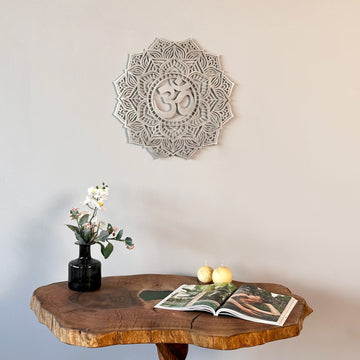 Silver OM mandala metal wall art above a live-edge wood table with an open magazine