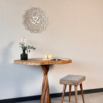 Silver OM mandala metal wall art above a pedestal table with a stool, medium view