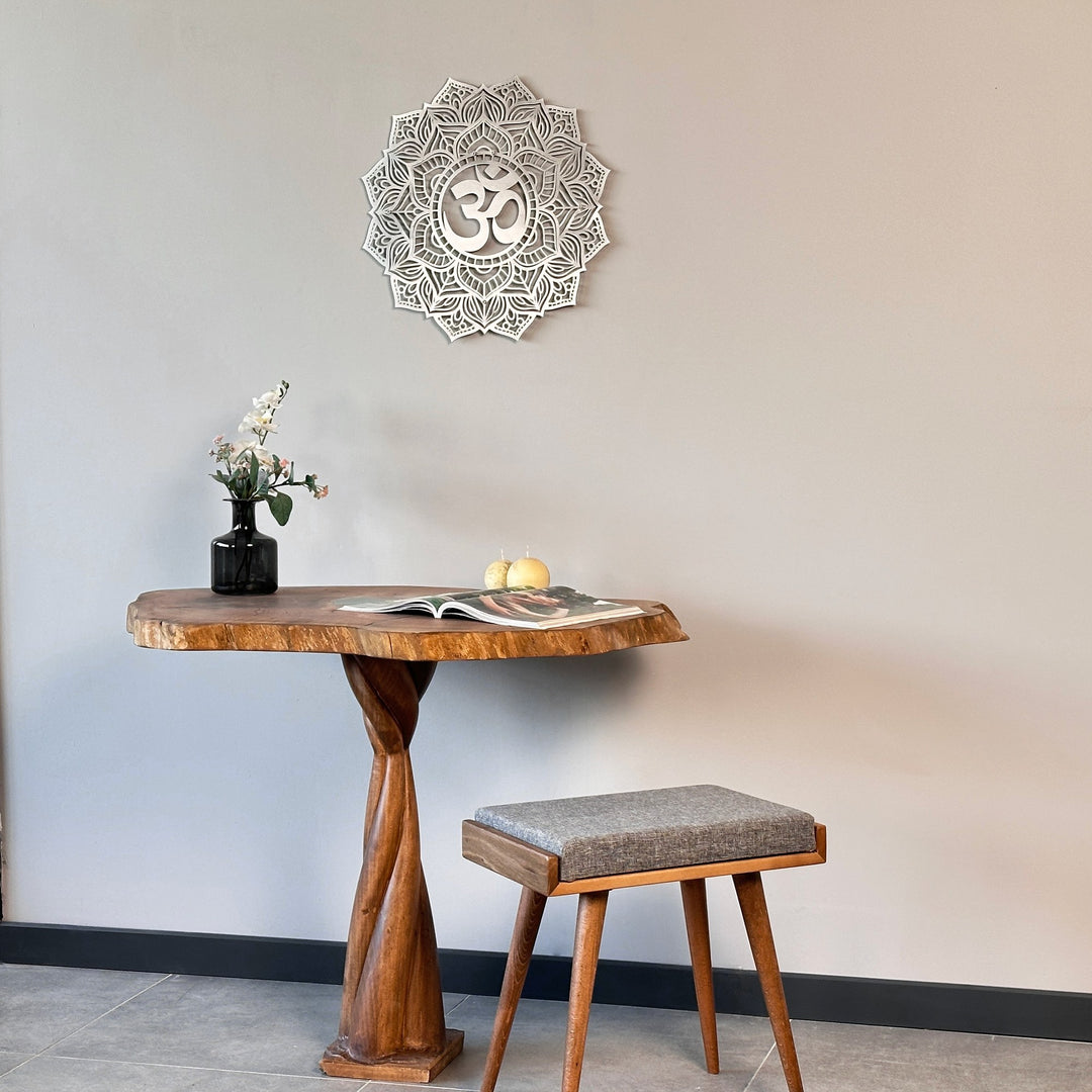 Small silver OM mandala metal wall art above a pedestal table with a gray stool, wide view