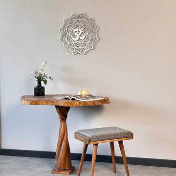 Small silver OM mandala metal wall art above a pedestal table with a gray stool, wide view