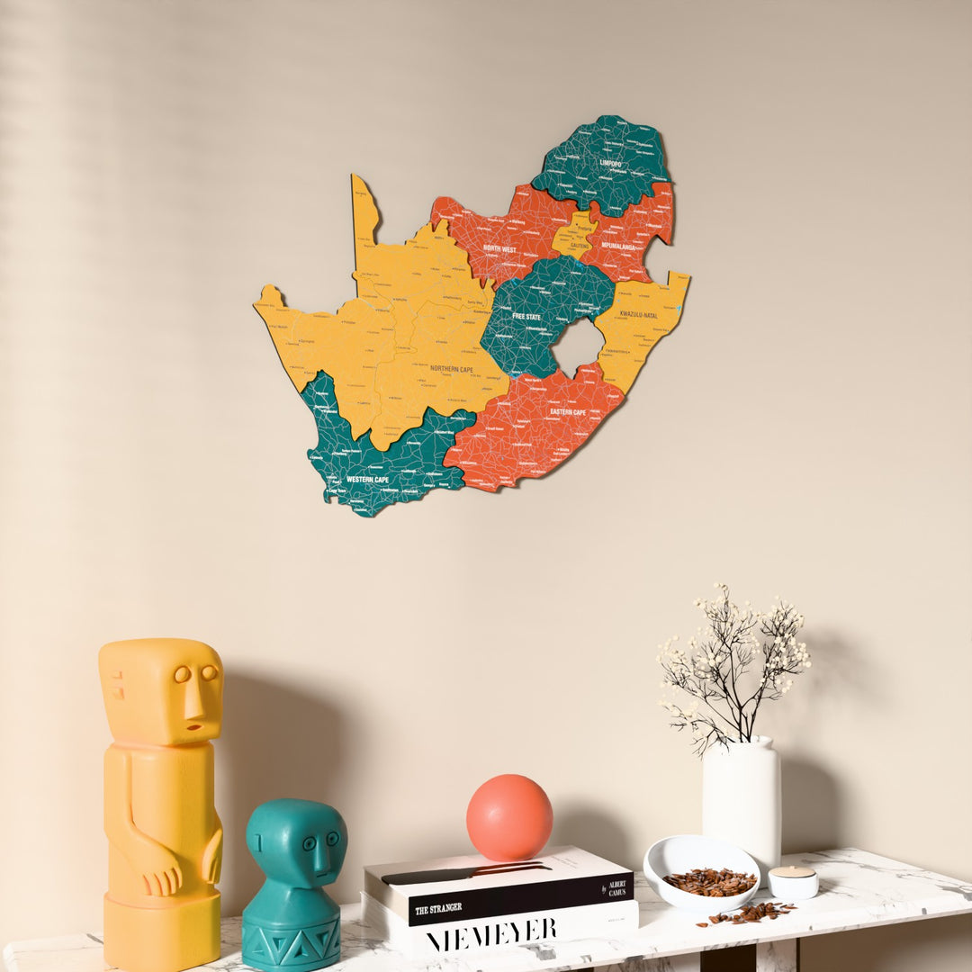 Flag colored South Africa wooden wall map on a beige wall above a console with figurines