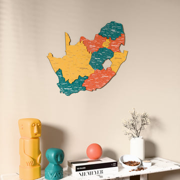 Flag colored South Africa wooden wall map on a beige wall above a console with figurines