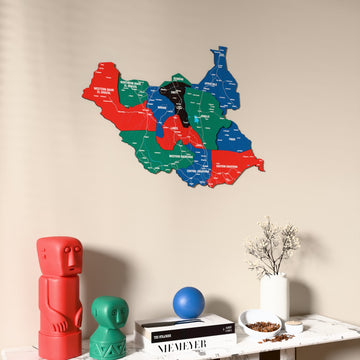 Flag colored South Sudan wooden wall map on a beige wall above a console with figurines