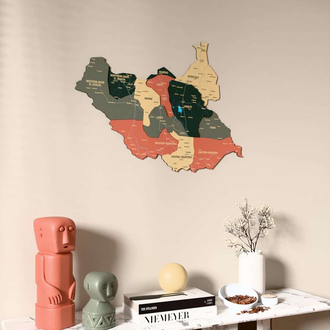 Sage South Sudan wooden wall map on a beige wall above a console with figurines