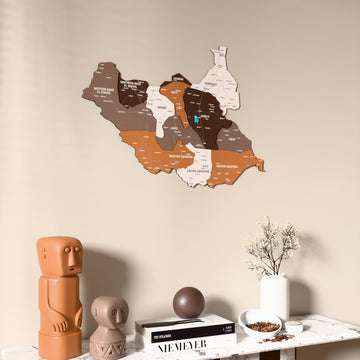Soil South Sudan wooden wall map on a beige wall above a console with figurines