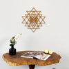 Metal wall art piece above a wooden table with decor items on a light gray background
