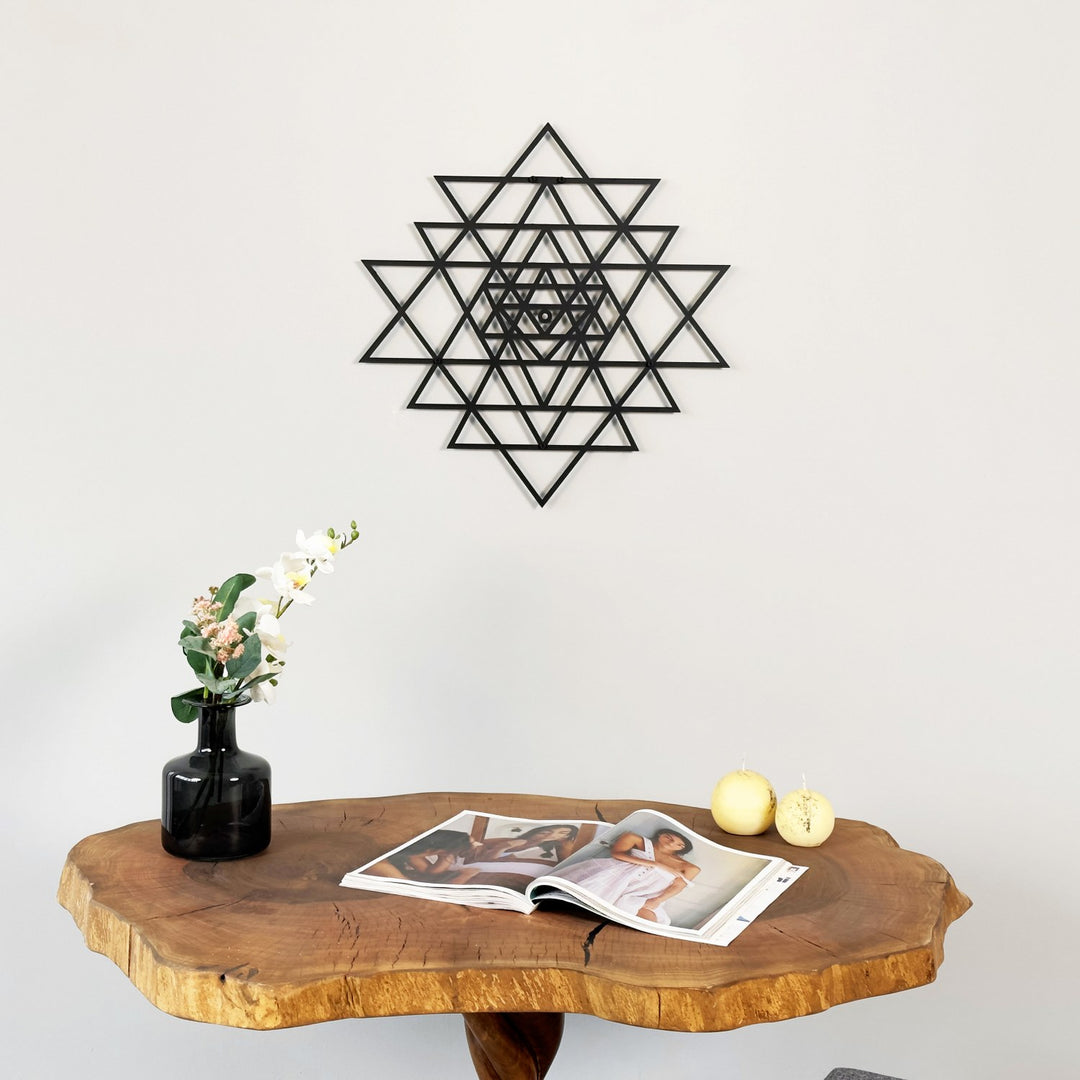 Decorative wall art with a geometric design above a wooden table with a magazine and decorative items.