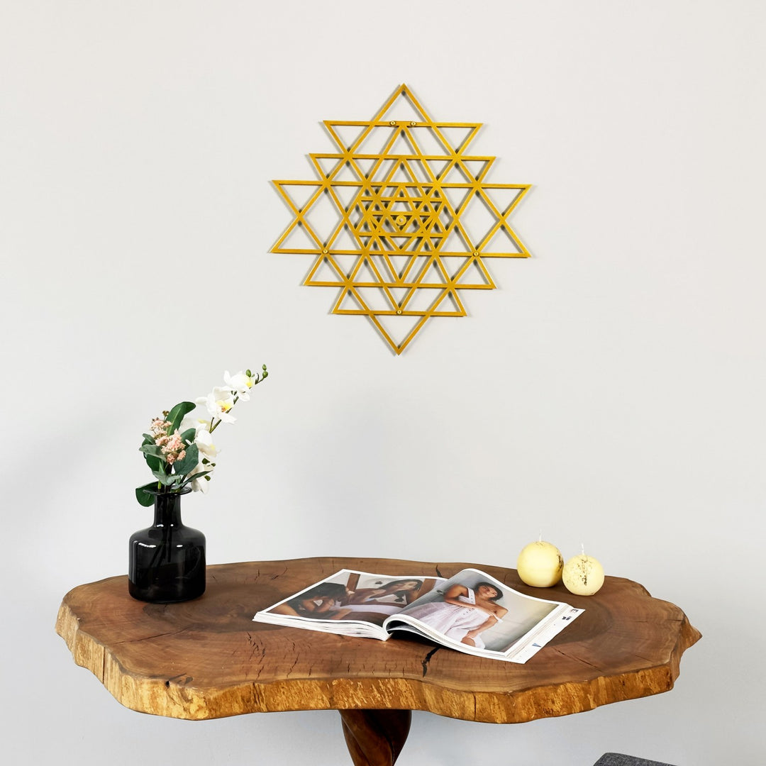 Wooden table with a magazine, vase, and decorative items against a white wall with a geometric wall art piece.