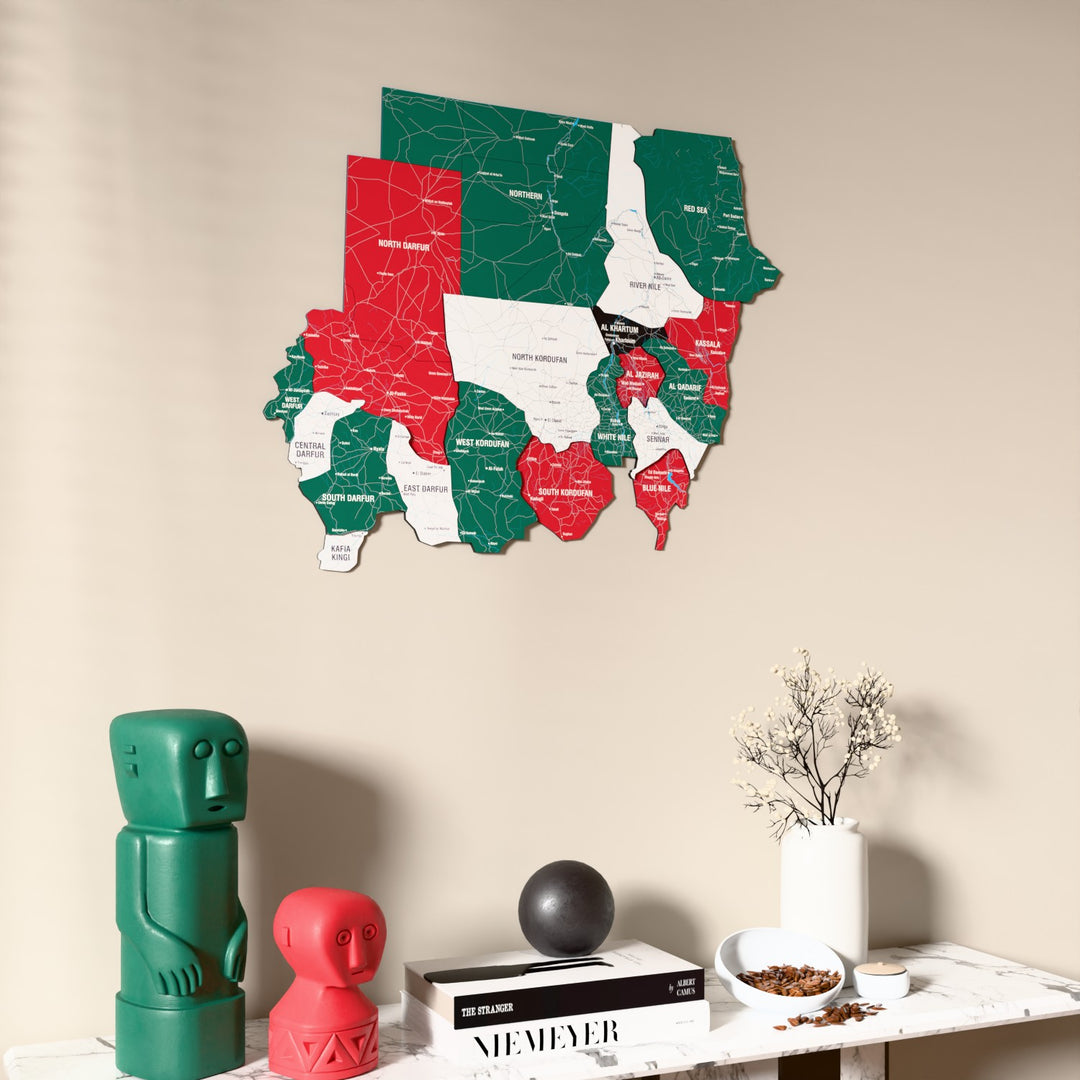 Flag colored Sudan wooden wall map on a beige wall above a console with figurines