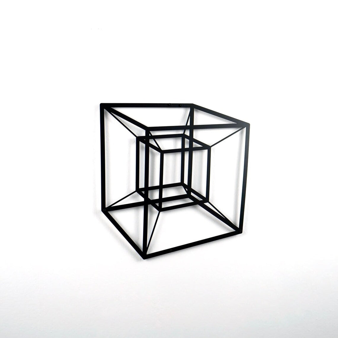 Black tesseract cube metal wall art on a white wall, side view