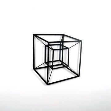 Black tesseract cube metal wall art on a white wall, side view