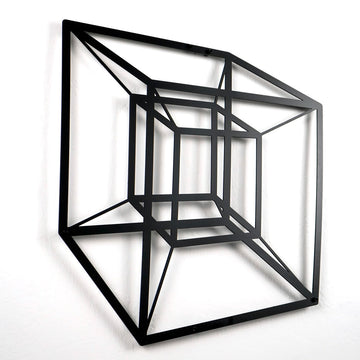 Black tesseract cube metal wall art on a white wall, close view