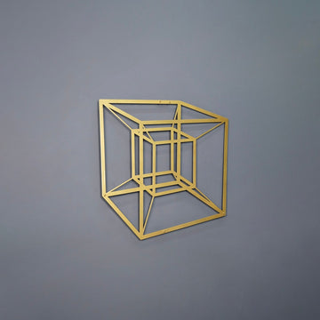 Gold tesseract cube metal wall art on a grey wall, side view