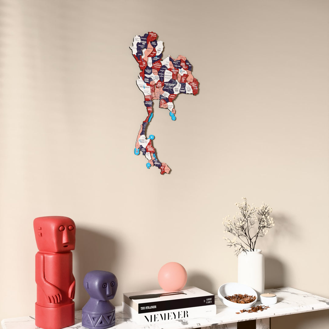 Flag colored Thailand wooden wall map on a beige wall above a console with figurines