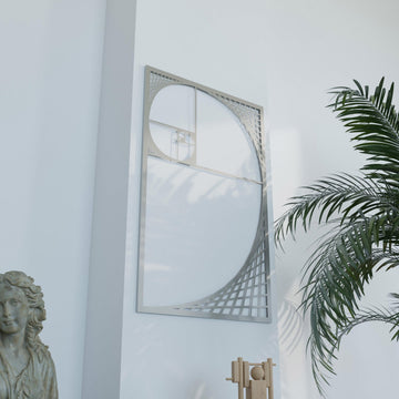 Silver Fibonacci spiral metal wall art, angled view with palm fronds at the right and a stone bust at the lower left