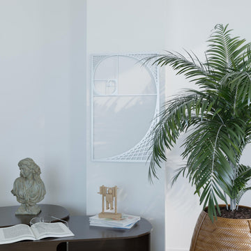 Silver Fibonacci spiral metal wall art on a white wall beside a palm and a stone bust, wide view