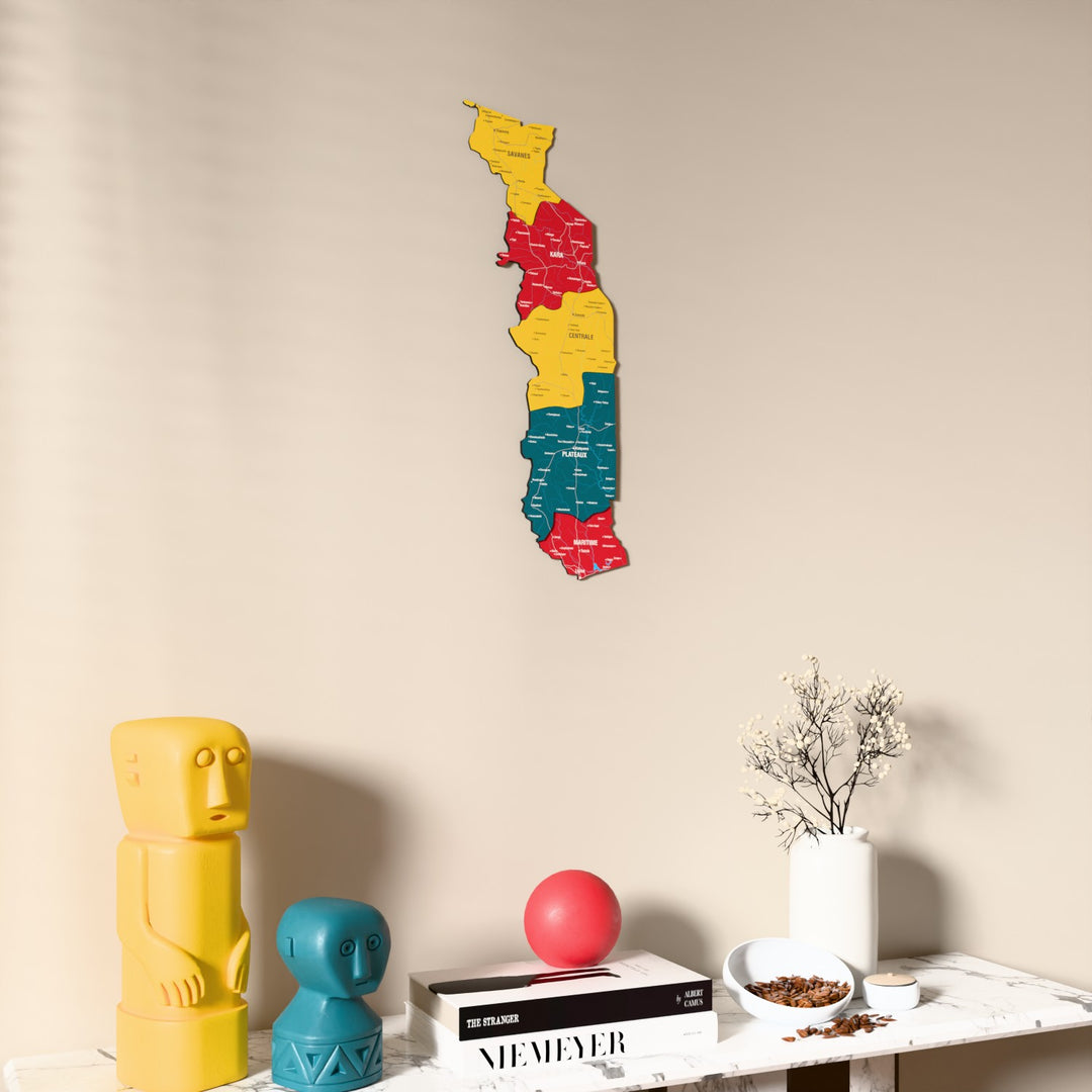 Flag colored Togo wooden wall map on a beige wall above a console with figurines