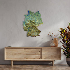 Topographic Germany metal wall map above a light wood sideboard with a vase