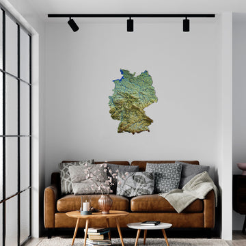 Topographic Germany metal wall map on a white wall above a brown leather sofa under track lights