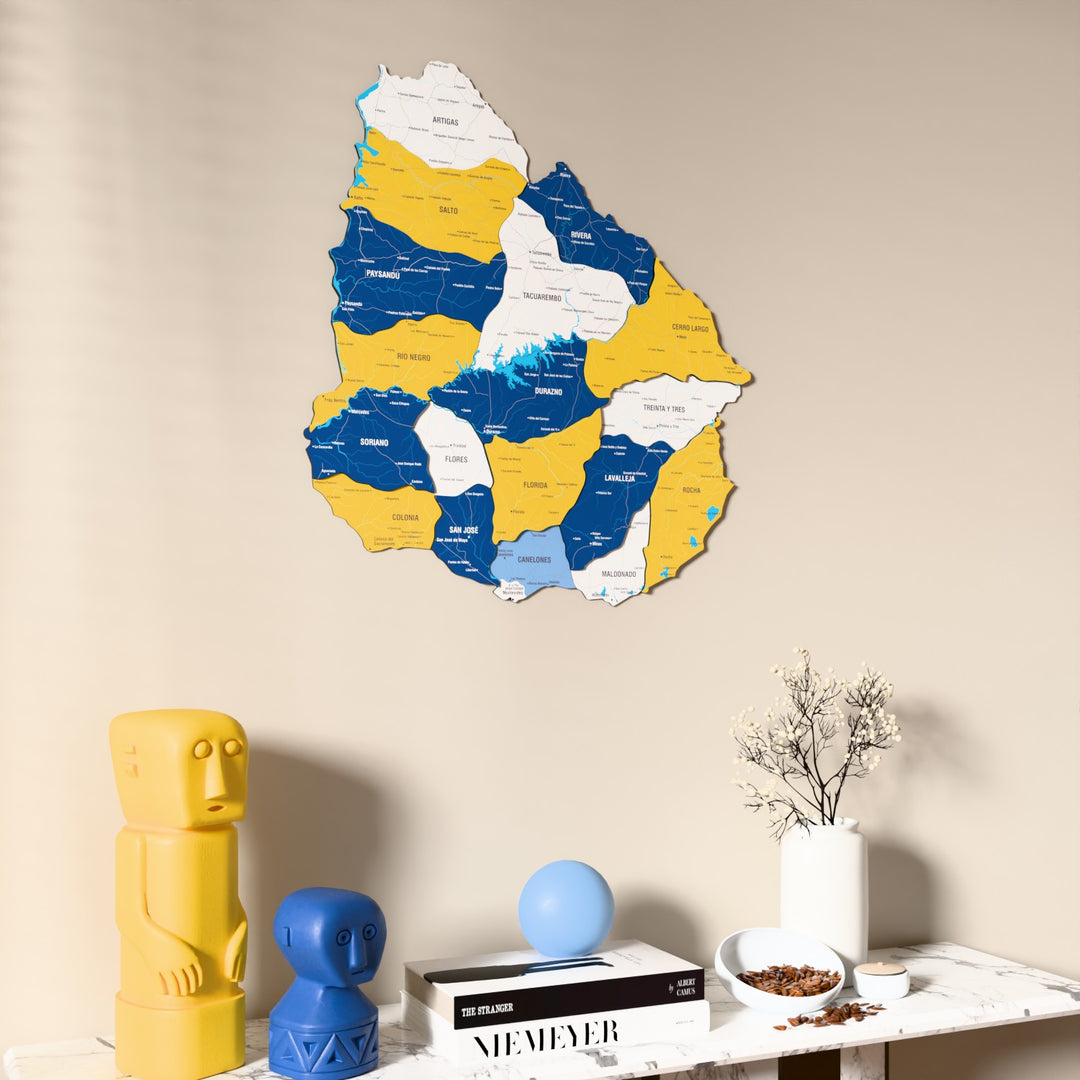 Flag colored Uruguay wooden wall map on a beige wall above a console with figurines