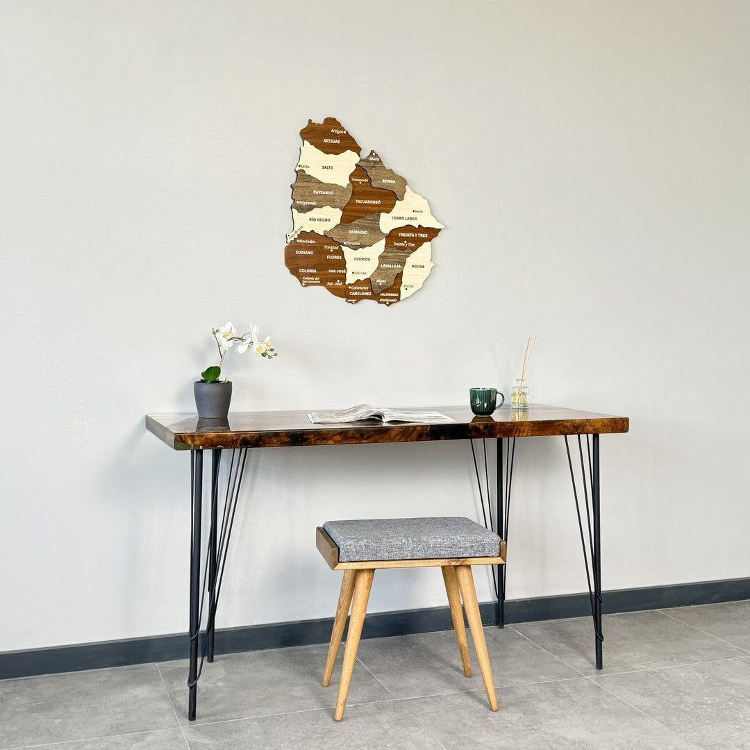 Uruguay wooden map centered above a narrow desk and stool, straight-on view