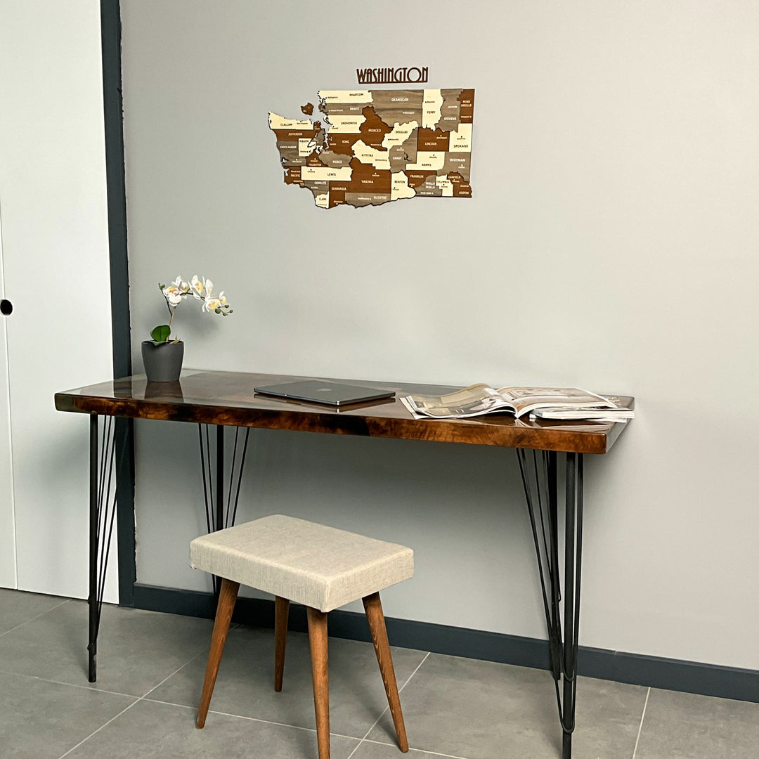 Washington State wooden wall map beside a white door, above a desk and cushioned stool