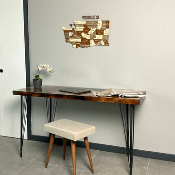 Washington State wooden wall map beside a white door, above a desk and cushioned stool