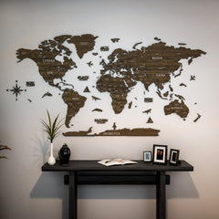 Betul wooden world map in dark brown wood above a black console with a vase and framed photos, wide view