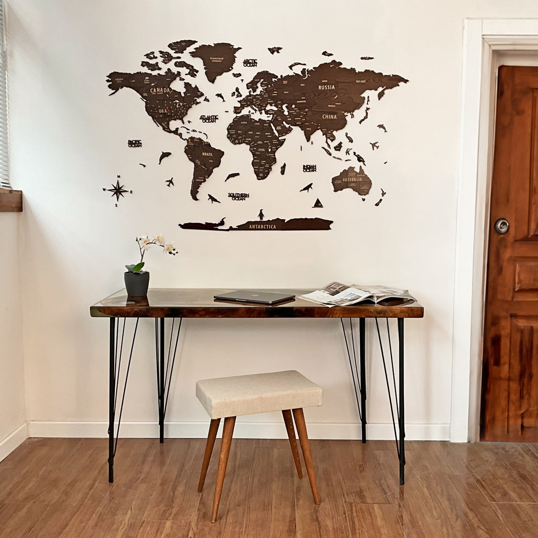 Dark brown wooden world map above a hairpin-leg desk and cream stool beside a wood door